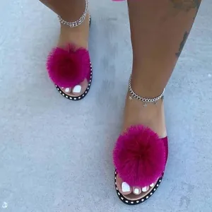 Detail view of stylish pink faux fur pom-pom slide sandals with studded sole edges.