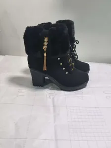 Side view of black high heel boots featuring faux fur trim and gold tassel detail.