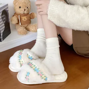 Close-up detail of cream fuzzy platform slippers featuring colorful floral embroidery for women
