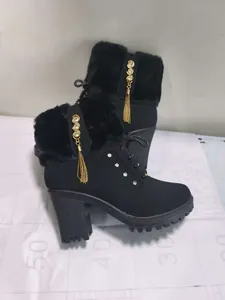 Close-up of black high-heeled winter boots with fur trim, gold tassels, and rhinestones