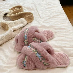 Detailed close-up of soft pink fuzzy slippers featuring beautiful floral embroidery on cross straps