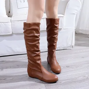 Slouchy brown mid-calf boots for women featuring a pleated design on grey wooden floor