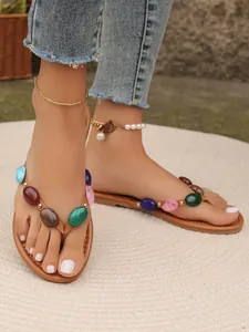 Detail von flachen Damen-Flip-Flops mit bunten Steinverzierungen auf den Riemen.