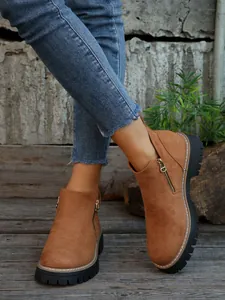Detailed close-up of brown suede ankle boots featuring side zipper and thick black sole