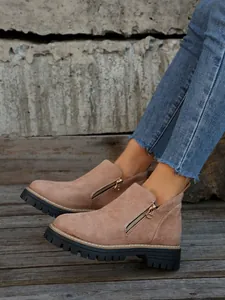 Close-up of suede ankle boots with side zipper and thick chunky soles on wooden floor