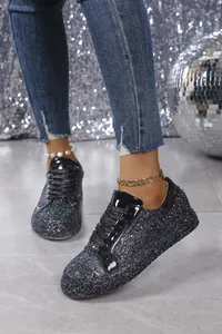 Close-up view of black glitter lace-up sneakers worn with jeans and shimmering background