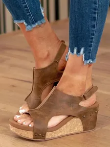 Detailed side view of brown leather platform wedge sandals with stylish rivet accents
