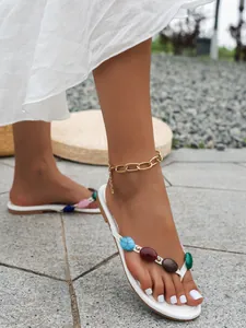 Detailaufnahme weißer flacher Flip-Flops mit bunten Steinen und goldener Fußkette