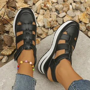 Close-up of black breathable hollow-out wedge sandals with velcro strap shown on feet.