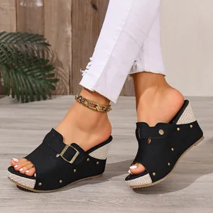 Close-up of stylish black wedge sandals with gold rivets and buckle detail worn by a model