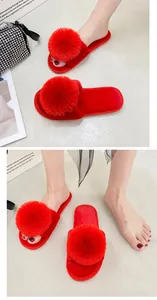 Détail de pantoufles en peluche rouge vif avec un grand pompon décoratif sur la bride.