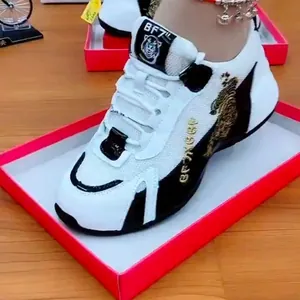 Nahaufnahme eines weiß-schwarzen Sneakers mit detailliertem goldenem Tiger-Stickmotiv.