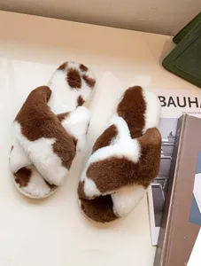 Primo piano di ciabatte incrociate in peluche con motivo a macchie di mucca marroni.