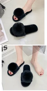 Vue détaillée des pantoufles en fausse fourrure noire avec pompon portées par le modèle
