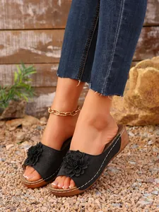 Gros plan détaillé de mules compensées noires pour femmes avec fleurs 3D et coutures