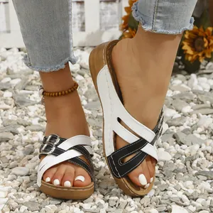 Detailed close-up of black and white cross-strap wedge sandals on a pebble surface