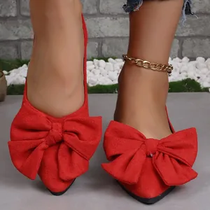 Primo piano di scarpe basse rosse a punta con grandi fiocchi decorativi in tessuto.