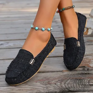 Close-up of black tweed loafers featuring a metal buckle on a rustic wooden floor