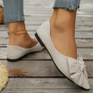 Dettaglio che mostra l'elegante fiocco e il design a punta delle scarpe piatte bianche.