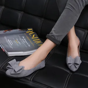 Close-up of grey suede flat shoes with an elegant butterfly bow on a black leather sofa