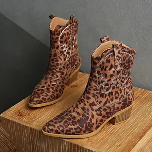 Detailed view of leopard print suede Western ankle boots on a rustic wood block.