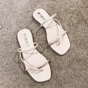 Eleganti sandali infradito piatti da donna color crema con sottili cinturini incrociati.