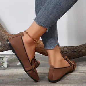 Detailed view of breathable brown fly-knit flat shoes with a bow decoration on feet