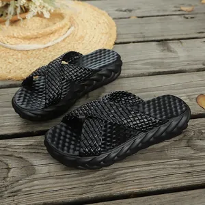 Dettaglio di ciabatte nere da donna con fascia a incrocio intrecciata e suola spessa.