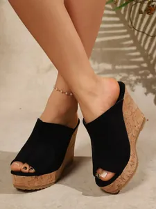 Elegantes mules de cuña en ante negro con punta abierta y suela de corcho natural.