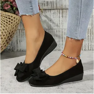 Close-up view of elegant black suede wedge pumps featuring a stylish bow detail on the toe