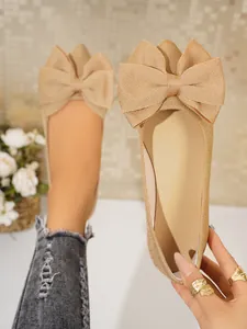 Close-up detail of golden glitter flat shoes with a large bow and square toe.