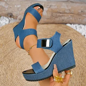 Nahaufnahme einer blauen Denim-Keilsandale mit Knöchelriemen und goldener Schnalle.