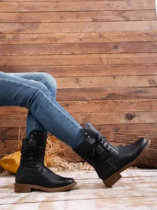 Schwarze Damen-Combat-Boots mit Nieten, gestylt mit Jeans vor Holzuntergrund