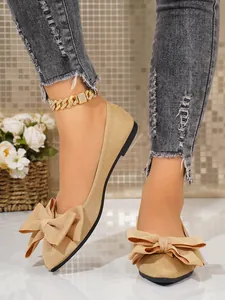 Elegant champagne gold square-toe ballet flats with large bow decoration shown on model's feet