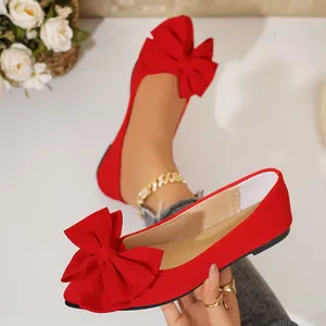 Close-up detail of elegant red flat shoes featuring a large decorative bow and pointed toe.