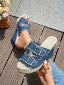 Nahaufnahme der blauen Denim-Keilsandaletten mit Fransen und silbernen Metallschnallen.