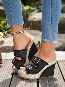 Detailansicht stilvoller schwarzer Denim-Keilsandalen mit Metallschnallen auf einer Holzterrasse