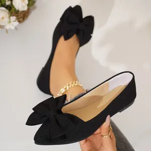 Close-up of elegant black pointed toe flats featuring a large decorative fabric bow.