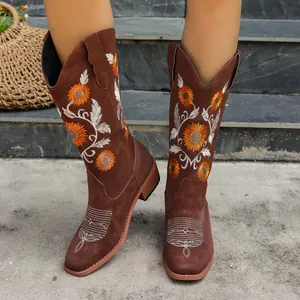 Close-up detail of brown cowboy boots with orange sunflower embroidery and chunky heel.