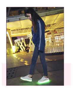White LED light-up sneakers glowing bright green while walking in a festive night street setting.