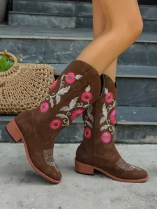 Close-up detail of brown tall boots featuring pink floral embroidery and chunky heels.