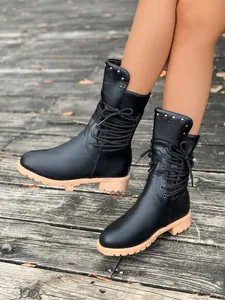 Detailaufnahme schwarzer Damen-Stiefeletten mit Nieten und Schnürung auf Holzdeck.