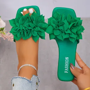 Close-up of green flat sandals with large decorative fabric flowers on square-toe footbed.