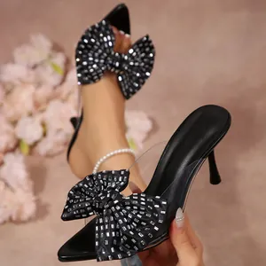 Détail de mules noires à bout pointu avec nœud en strass et bride transparente.