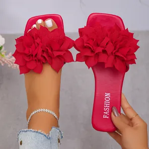 Close-up of red flat square-toe slippers with large vibrant fabric flower decorations.