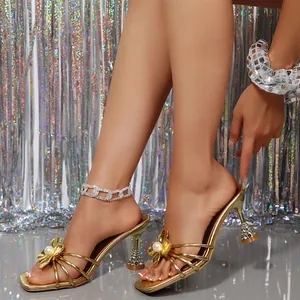 Détail de mules dorées à talons hauts avec une fleur en perle et un talon cristal