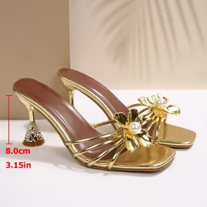 Vue détaillée de sandales dorées à talons avec décor de fleur en perle et talon de 8 cm.