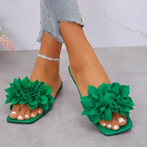Detail view of women's green flat slippers featuring a large fabric flower and square toe design