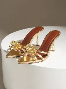 Détail de sandales dorées à talons hauts avec décoration florale en métal 3D élégante.