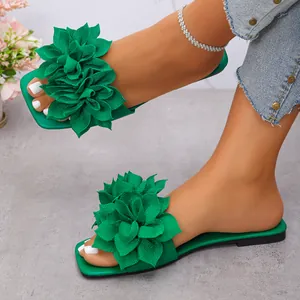 Close-up of green women's flat sandals with stylish large fabric flower decorations.